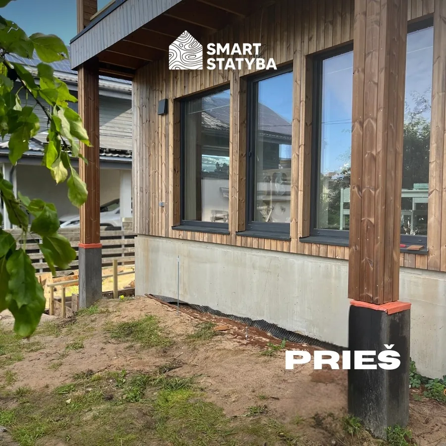 Before: bare sand and gravel along the concrete foundation of a timber-clad house, where the terrace is about to be built. Marked PRIEŠ.